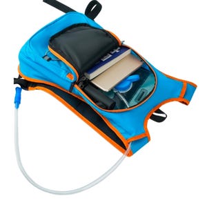 Op de afbeelding: Een blauwe hydratatierugzak met oranje afwerking, met een zwart vak en een doorzichtig waterreservoir. De rugzak heeft een doorzichtige buis met een blauw mondstuk. In de open zak zitten een boek en een tablet.