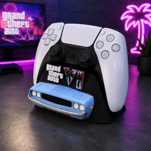 Op de afbeelding: Een zwart-witte standaard voor een videogamecontroller met een lichtblauwe voorbumper van een auto aan de basis en het Grand Theft Auto VI-logo in witte en roze tekst met zwarte palmbomsilhouetten op de voorkant van de zwarte steunstructuur.