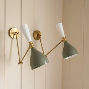 May include: Two wall sconces in a mid-century modern style. Each has a white, cone-shaped top and a green, bell-shaped shade with small white dots. The fixtures have brass-coloured arms and circular wall mounts.