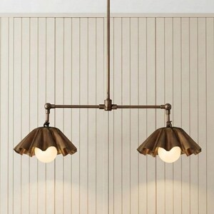 May include: A bronze-toned metal pendant light fixture featuring a central vertical rod connected to a horizontal bar with two adjustable arms. Each arm holds a fluted, bell-shaped shade in a matching bronze finish with a round white glass bulb.