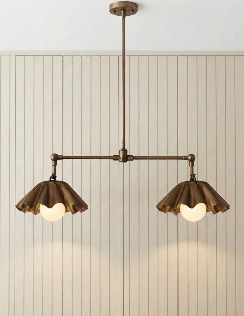 May include: A bronze-toned metal pendant light fixture featuring a central vertical rod connected to a horizontal bar with two adjustable arms. Each arm holds a fluted, bell-shaped shade in a matching bronze finish with a round white glass bulb.