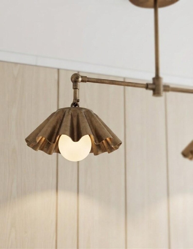May include: A ceiling-mounted light fixture featuring a metallic bronze finish with a horizontal arm and a downward-facing, pleated, bell-shaped shade. A single, spherical, frosted white glass bulb is centered within the fluted metal shade.