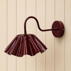 May include: A dark burgundy wall lamp featuring a curved metal arm and a wide, pleated, bell-shaped shade. The fixture is mounted on a circular base, with a glossy finish throughout the entire structure, providing a focused downward light.
