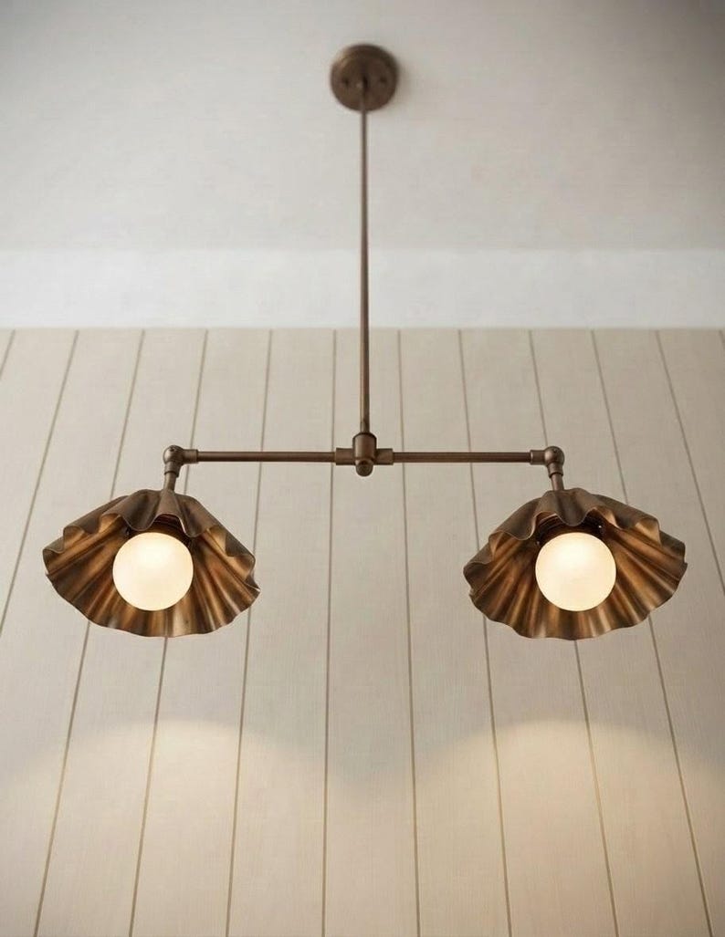 May include: A bronze-toned metal pendant light fixture featuring a central rod suspended from a circular ceiling mount. The fixture has two horizontal arms, each ending in a scalloped, shell-shaped shade containing a round, frosted white light bulb.