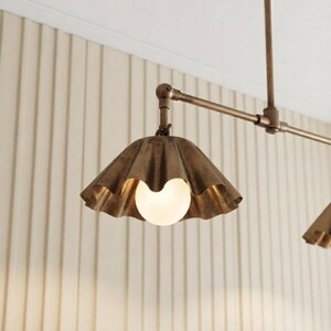 May include: A ceiling-mounted light fixture featuring a metallic bronze finish with a horizontal arm and a scalloped, bell-shaped shade. A single round, frosted white glass bulb is centered within the shade, emitting a soft, warm glow.