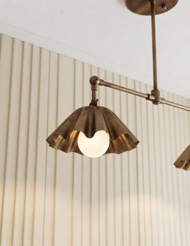 May include: A ceiling-mounted light fixture featuring a metallic bronze finish with a horizontal arm and a scalloped, bell-shaped shade. A single round, frosted white glass bulb is centered within the shade, emitting a soft, warm glow.