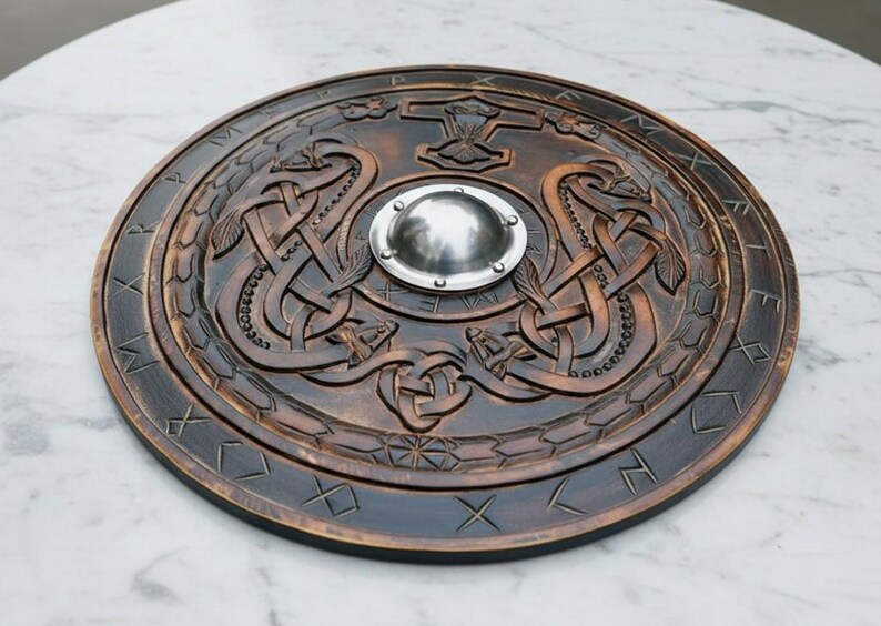May include: A round, wooden shield with intricate carvings. The shield features a central metal boss, a hammer symbol, and intertwined serpent designs. The outer rim has etched runes. The shield is a dark brown color.