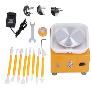 May include: A yellow and white pottery wheel with a silver spinning surface, a set of sculpting tools, and various power adapters. The wheel has an "ON" switch and is designed for ceramic art projects.