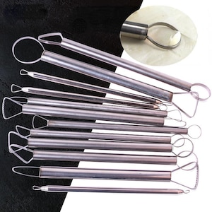 May include: A set of stainless steel pottery tools, including loop tools, ribbon tools, and wire tools. The tools have cylindrical handles and various shaped heads for sculpting and shaping clay. The tools are designed for use in pottery, ceramics, and sculpting projects.