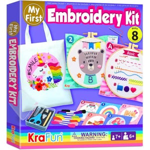 May include: A KraFun My First Embroidery Kit box featuring a white tote bag with a unicorn graphic, two wooden embroidery hoops with bear and basic stitch designs, colorful embroidery thread, a clear plastic case with scissors, and instruction cards.