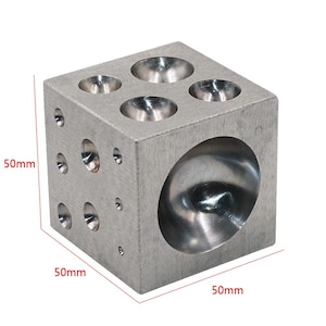 May include: A silver-colored metal dapping block cube featuring multiple hemispherical depressions of varying sizes on its top and side faces. The block is a cube with dimensions clearly labeled as 50mm by 50mm by 50mm on the image.