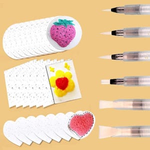 May include: A craft set featuring multiple white paper shapes including circles with a pink strawberry print, rectangles with a yellow flower print, and hearts with a pink heart print, accompanied by six clear water brushes with white bristles.