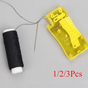 May include: A black sewing thread spool, a silver sewing needle, and a yellow plastic automatic needle threader device. The thread is connected from the spool through the needle eye. The text 1/2/3Pcs is printed in red at the bottom right.