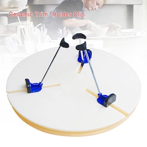 May include: A white circular ceramic trim holder clip tool featuring three adjustable metal arms with black curved grips and blue plastic bases, designed for pottery centering. The text Ceramic Trim Holder Clip is visible.