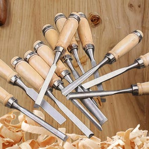 May include: A collection of wood chisels with wooden handles and silver blades. The chisels are arranged on a wooden surface with wood shavings scattered around. The handles are light brown, and the blades are various shapes.
