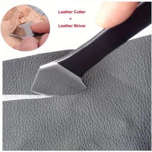 May include: A leather skiving tool with a black handle and a silver blade is shown in use on a piece of gray leather. The text "Leather Cutter + Leather Skiver" is in the upper left corner. The tool is used to thin the leather.