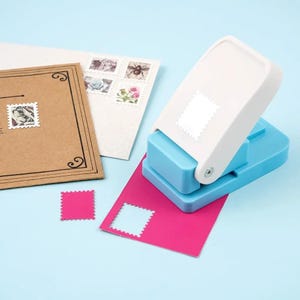 May include: A blue and white stamp punch with a pink paper and a cut-out stamp. There are also stamps on a brown envelope and a white card. The background is light blue.