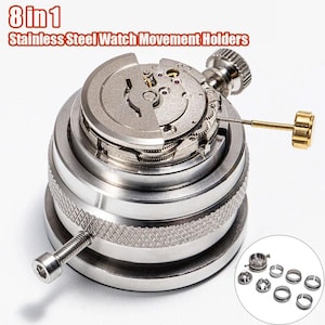 May include: Stainless steel watch movement holder with 8-in-1 functionality. The tool is silver with a screw and a gold-colored adjustment knob. The watch movement is partially disassembled, revealing intricate gears. A set of small silver rings is included.