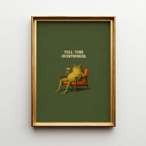 May include: Framed art print. A green frog, holding a cocktail, sits in an armchair against a dark green backdrop. Text reads "FULL-TIME OVERTHINKER.". The print has a gold frame.