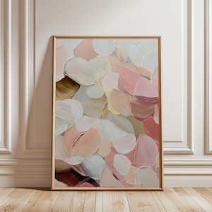 May include: Abstract art print in a wooden frame. The artwork features layered brushstrokes in white, pink, beige, and brown. The painting is displayed against a white wall and wooden floor.