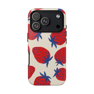 Peut inclure: Coque de téléphone avec un motif répété de fraises rouges avec des tiges et des feuilles bleues sur un fond crème. Le boîtier a un module caméra noir et des accents latéraux noirs.