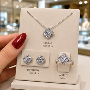 Puede incluir: Un conjunto de joyería plateada que incluye un collar, un par de pendientes y un anillo, cada uno con un diseño de nudo y piedras claras. El colgante mide 1 cm x 1 cm, los pendientes 1 cm x 1 cm y el anillo mide 1,5 cm de diámetro.