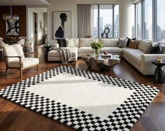 May include: A large, rectangular area rug with a white center and a black and white checkered border. The rug is placed on a dark wood floor in a modern living room setting. The room features a large sectional sofa and a coffee table.