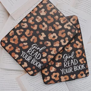 Op de afbeelding: Twee zwarte e-reader covers met een luipaardprint in bruin en beige, en de tekst "Girl Read Your Book" in het wit. De covers liggen op open boeken.