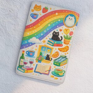 Op de afbeelding: Een witte Kindle-hoes met een kleurrijk ontwerp met een regenboog, katten, boeken, koffiekopjes en voedselillustraties. De hoes heeft een grillige, geïllustreerde stijl.