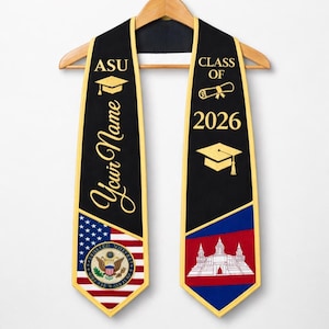 Peut inclure: Écharpe de remise de diplôme noire avec bordure dorée, affichant "ASU" et "Your Name" d'un côté, et "Class of 2026" de l'autre. Ornée d'un chapeau de remise de diplôme, d'un parchemin et de drapeaux. L'écharpe est suspendue à un cintre en bois.