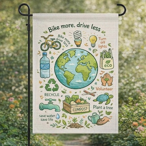 Op de afbeelding: Een tuinvaandel met een groene en blauwe illustratie van de aarde, omringd door milieuvriendelijke iconen en tekst. De vlag leest "Bike more, drive less" en promoot recycling, composteren en vrijwilligerswerk. De vlag hangt aan een zwarte metalen standaard.
