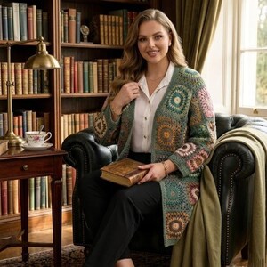 May include: A colorful, open-front crochet cardigan with square patterns in shades of green, brown, and pink. The cardigan is worn over a white blouse and black pants. The person is seated in a leather armchair, holding a vintage book.