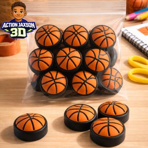 May include: A collection of small, round basketball-themed tokens, each featuring an orange textured surface with black lines, set within a black circular base. Several tokens are contained in a clear plastic bag, while others sit outside.