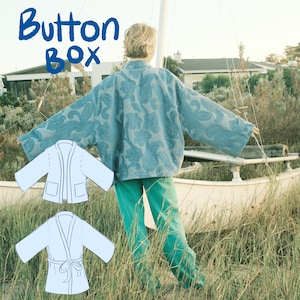 Può includere: Una persona indossa una giacca turchese con motivo paisley e pantaloni turchesi. Il testo "Button Box" è in blu in alto a sinistra. Due modelli di giacca azzurra sono in basso a sinistra.