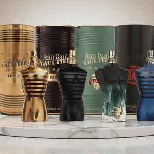 Könnte beinhalten: Eine Sammlung von Jean Paul Gaultier Düften. Die Flakons in Torsoform sind in Gold, Schwarz und Blau erhältlich. Die Verpackung umfasst zylindrische Behälter mit dem Markennamen und dem Duftnamen.