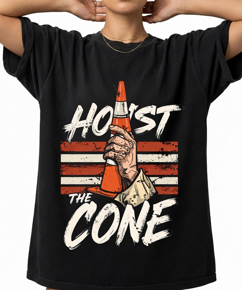 Puede incluir: Camiseta negra con las palabras blancas "HOIST THE CONE". El dise&ntilde;o presenta una mano sosteniendo un cono de tr&aacute;fico naranja sobre un fondo de rayas rojas y blancas.