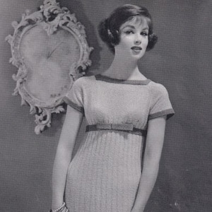 May include: A vintage monochrome photograph of a woman in a light-coloured knitted dress with short sleeves, a bow at the waist, and a knee-length skirt. She is wearing gloves and heels. A decorative clock is in the background.