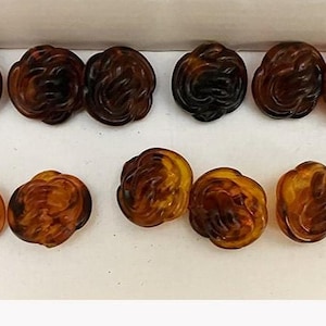 May include: Ten brown plastic buttons with a rose design. The buttons are arranged in two rows of five.