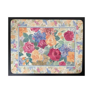 May include: Rectangular floral placemat featuring a vibrant arrangement of roses and hydrangeas in shades of pink, yellow, and blue. The placemat has a cream-colored background with a floral border and a black edge.