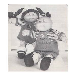 May include: Two vintage Cabbage Patch Kids dolls. One doll wears a knitted red and white striped sweater and overalls. The other doll wears a knitted dress and hat. Both dolls have yarn hair and are wearing knitted shoes.