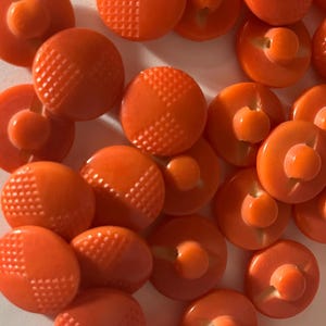 May include: A collection of 20 orange plastic buttons with a textured design. The buttons have a two-hole shank.