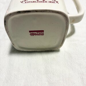 May include: Cream-colored ceramic pitcher with a handle, featuring the text "JOHNNIE WALKER ESTABLISHED 1820" in red. The bottom of the pitcher has the text "WADE PDM MADE IN ENGLAND".