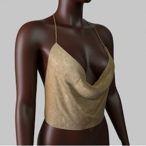 以下が含まれることがあります： 深いVネックのゴールドカラーのホルタートップ。 トップは、チェーンメイルのような光沢のある素材で作られています。 ストラップは細く繊細で、生地はエレガントにドレープされています。