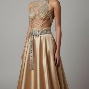 May include: A gold satin skirt paired with a sparkling rhinestone belt and a halter top made of draped silver chains. The top covers the chest and neck, creating a glamorous and elegant look. The outfit is perfect for a special occasion.