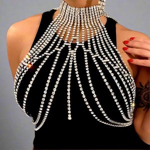 以下が含まれることがあります： キラキラ光るラインストーンで飾られた黒のホルターネックトップ。ハイネックで、前面に流れるようにあしらわれたラインストーンのディテールが特徴です。デザインは人目を引き、華やかで、特別な機会に最適です。