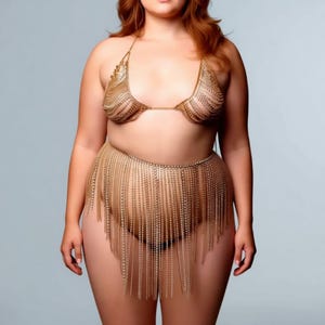 以下が含まれることがあります： ゴールドカラーのチェーンメイルビキニセット。トップスはホルターネック、ボトムは長いチェーンが付いたスカートです。小さな金属片が繋がって作られており、キラキラとした輝きを放っています。背景は無地のライトグレーです。