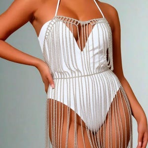 以下が含まれることがあります： 白いホルターネックボディスーツ、シルバービーズフリンジ付き。 ボディスーツは深いVネックラインとウエストとネックラインの周りのビーズアクセントが特徴で、長いビーズフリンジが前面に流れ落ちています。