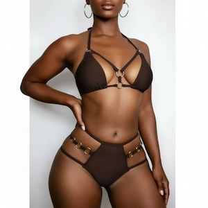 以下が含まれることがあります： ホルターネックのトップスとハイウエストのボトムスが特徴の茶色のビキニセット。トップスの中央にはリングのディテールがあり、ボトムスにはサイドにリングのアクセントがあります。水着は滑らかな無地の生地で作られています。