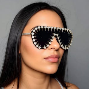 May include: Black aviator sunglasses with gold frames and a decorative rim of sparkling crystals and spikes. The lenses are dark, and the overall design is glamorous and eye-catching.
