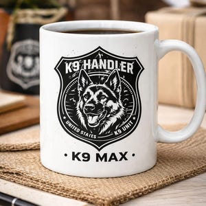 May include: White ceramic mug featuring a black and white graphic of a German Shepherd dog within a shield design. The text "K9 Handler" and "K9 Unit United States" are displayed. The mug also has the text "K9 MAX".